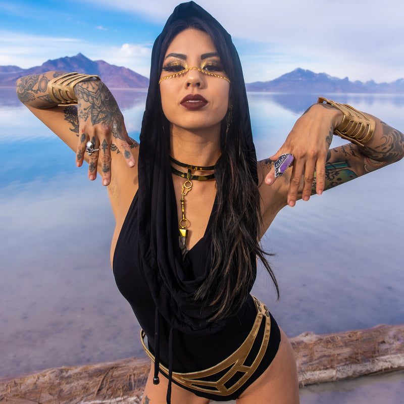 Phoenix Fireflow wearing a black hooded cowl bodysuit with gold leather accessories, perfect for Envision Festival or Burning Man.
