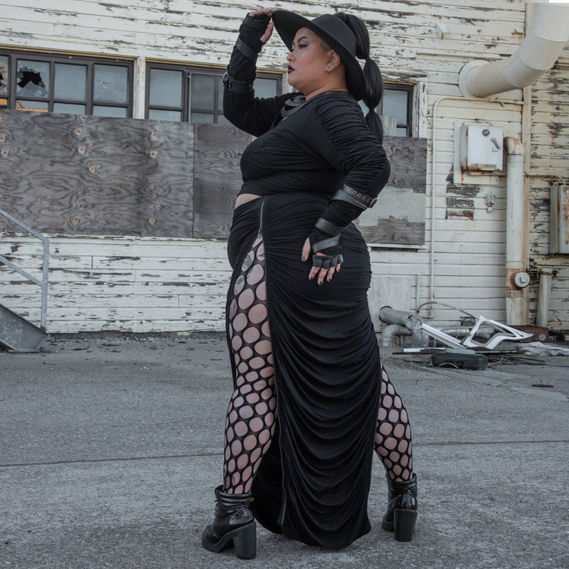 Kitty Kapow in our plus sized dark streetwear, standing in an industrial area wearing fish net tights.